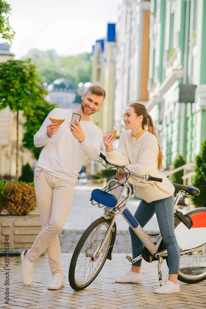 Man taking selfie on smartphone with woman on bicycle.