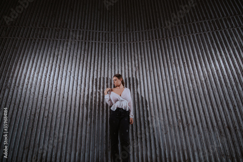 A beautiful young caucasian girl in a white shirt stands in front of a ribbed wall