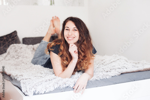 Young pretty woman at home, laying on a ned, looking at the camera and smiling photo