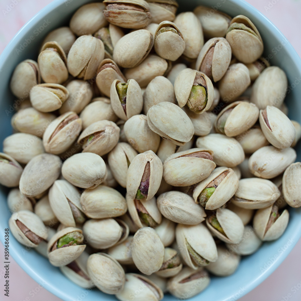 Roasted salted pistachios in shell in bowl on pink background, concept of healthy eating vegan food. Top view, close up, selective focus, copy space