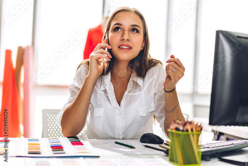 Portrait of young beautiful pretty woman fashion designer stylish sitting and working.Attractive young girl use desktop conputer and colorful fabrics at fashion design studio photo