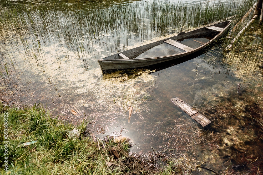 Old sunken wooden boat on lake in thicket of grass Old sunken wooden boat on lake in thicket of grass