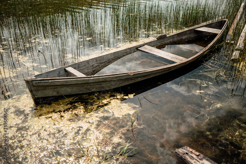 Old sunken wooden boat on lake in thicket of grass