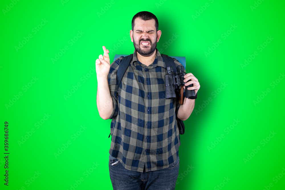 Closeup portrait young bearded traveler man praying hands clasped hoping for best asking for forgiveness or miracle isolated green wall background. Human emotion facial expression feeling