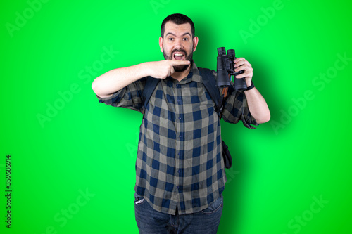 Young traveler man pointing and looking at copy space. Handsome young businessman isolated on green background