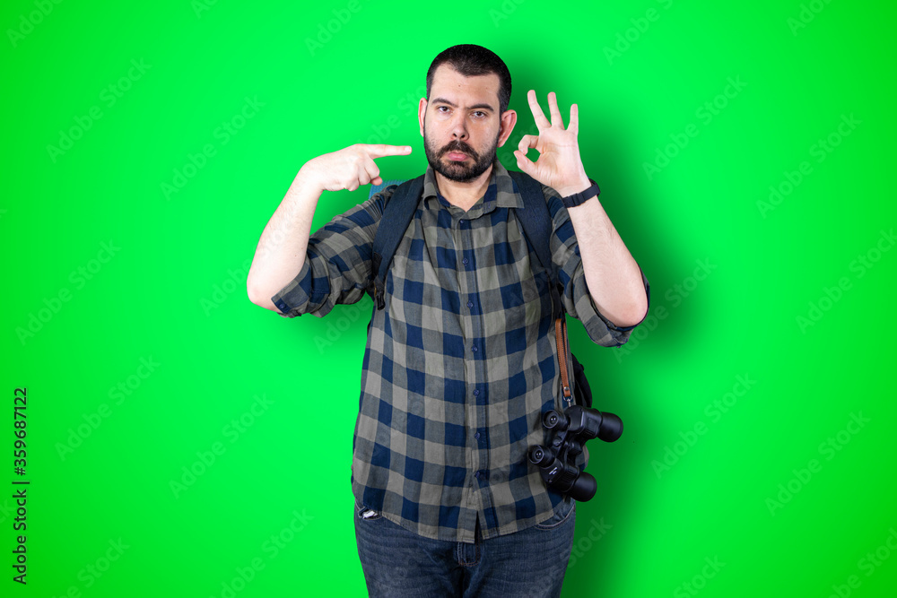 Young traveler man pointing and looking at copy space. Handsome young businessman isolated on green background Young traveler man pointing and looking at copy space. Handsome young businessman isolated on green background