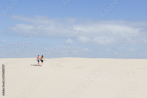 Rear view of caucasian couple walking hand in hand up sand dune.