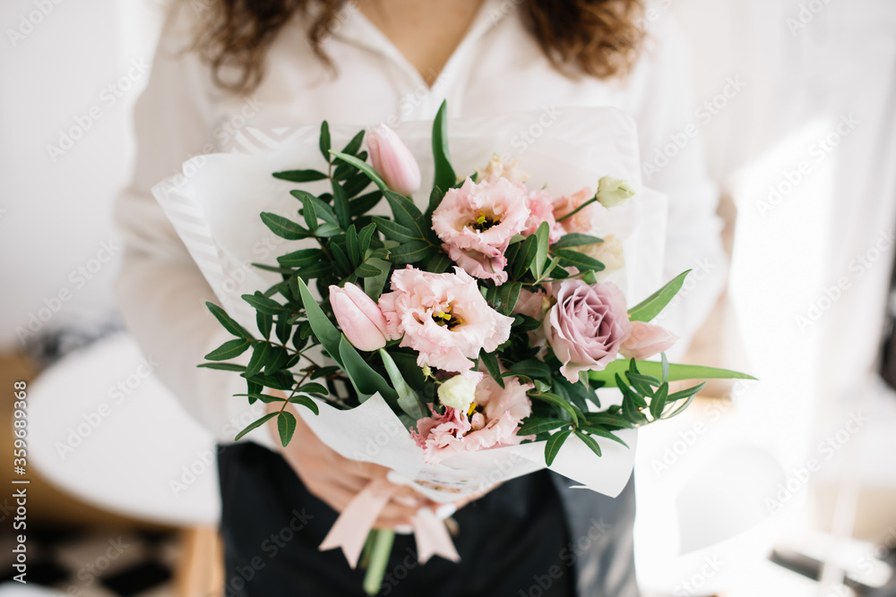 Very nice young woman holding huge beautiful blossoming bouquet of fresh roses, eustoma, pistachio, tulips in pink color on the grey background