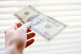 Hand with a 100 dollar bill on a background of white bright shutters.