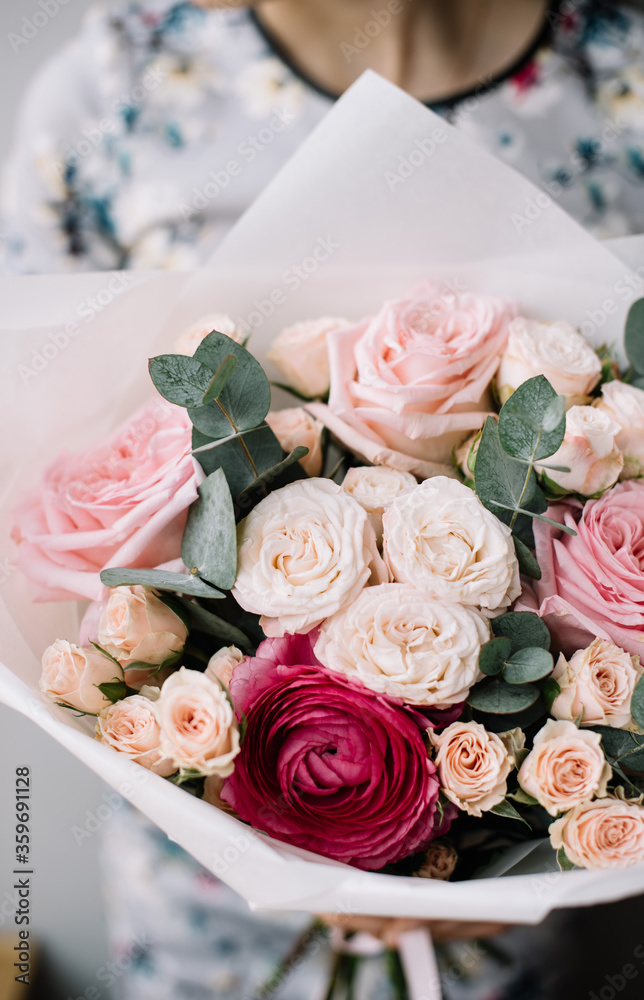 Very nice young woman holding beautiful blossoming bouquet of fresh roses, ranunculus, eucalyptus in pink colors on the grey background Very nice young woman holding beautiful blossoming bouquet of fresh roses, ranunculus, eucalyptus in pink colors on the grey background