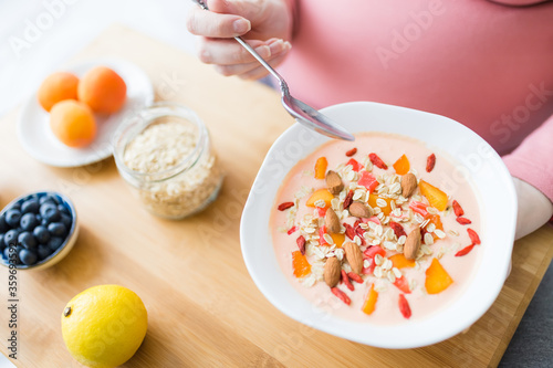 Close up of young pregnant woman sitting on bed and eating granola with cereals and yogurt.