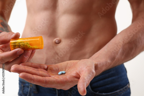 Close up of shirtless muscular man holding bottle of vitamins