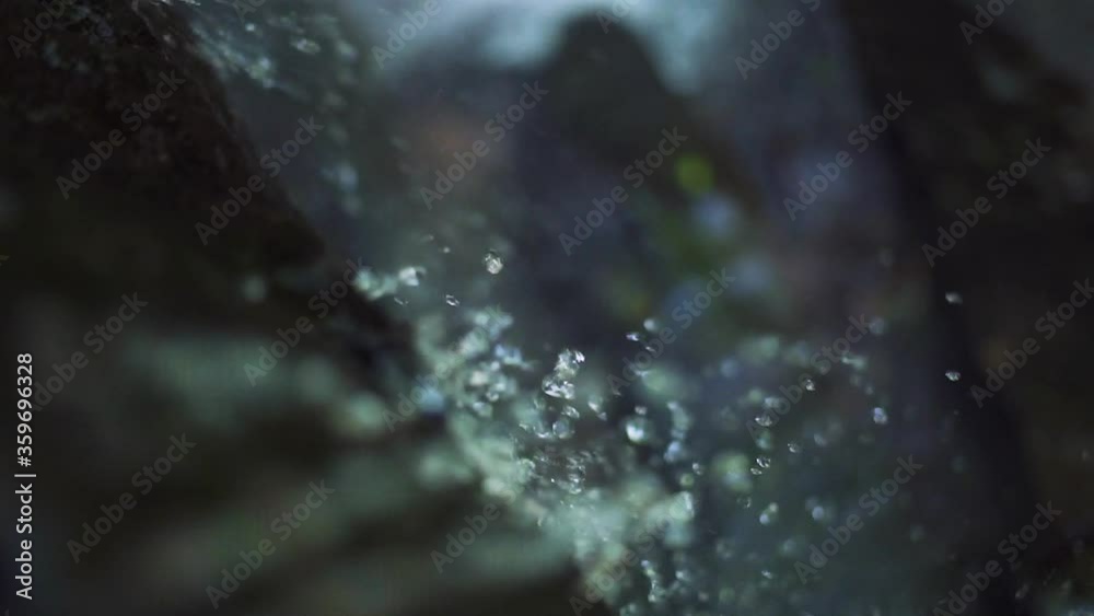 Close up view at a waterfall water droplets and spray flowing and splashing on rocks. Above waterfall angle. Outdoor, nature concept.