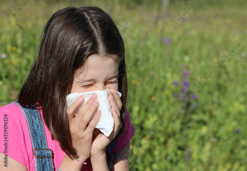 young girl sneezes and blows her nose with white handkerchief