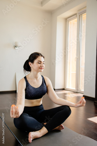 Home yoga. Young woman relaxing in her living room meditating on fitness mat. Leisure, self development, mental health and contemplation