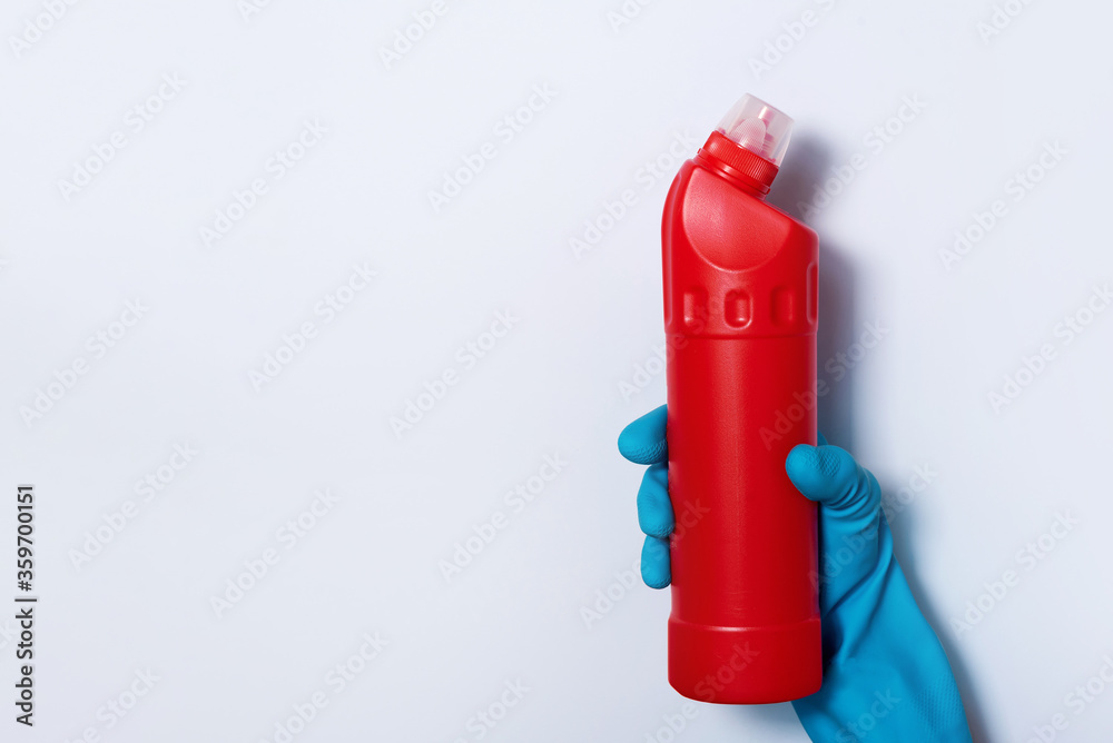 Hand in glove holding white plastic bottle of cleaning product, household chemicals. Copy space. Cleaning service concept. Household chemical cleaning products, brushes and supplies. Detergent bottle Hand in glove holding white plastic bottle of cleaning product, household chemicals. Copy space. Cleaning service concept. Household chemical cleaning products, brushes and supplies. Detergent bottle