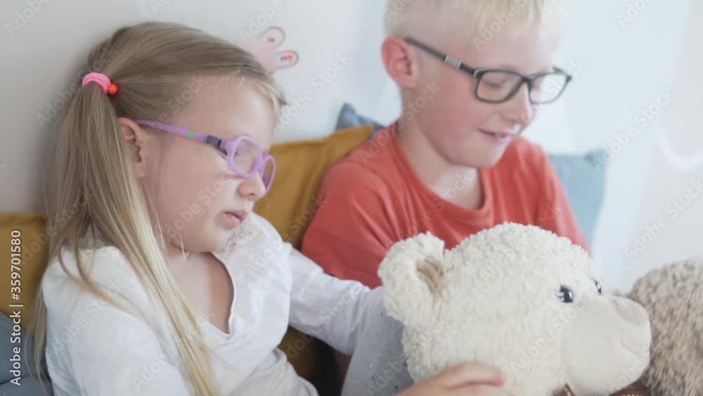 A boy and a girl with glasses play with toys teddy bear at home on the bed. A boy and a girl with glasses play with toys teddy bear at home on the bed.