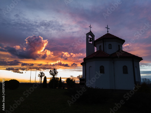 A silhouette of religious building in the countryside against colorful clouds at sunset.