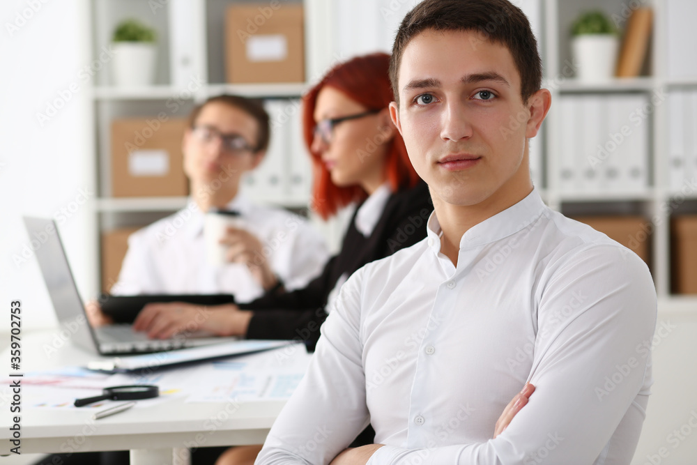 Obraz premium Serious gentleman in white shirt looking at camera while coworkers using laptop