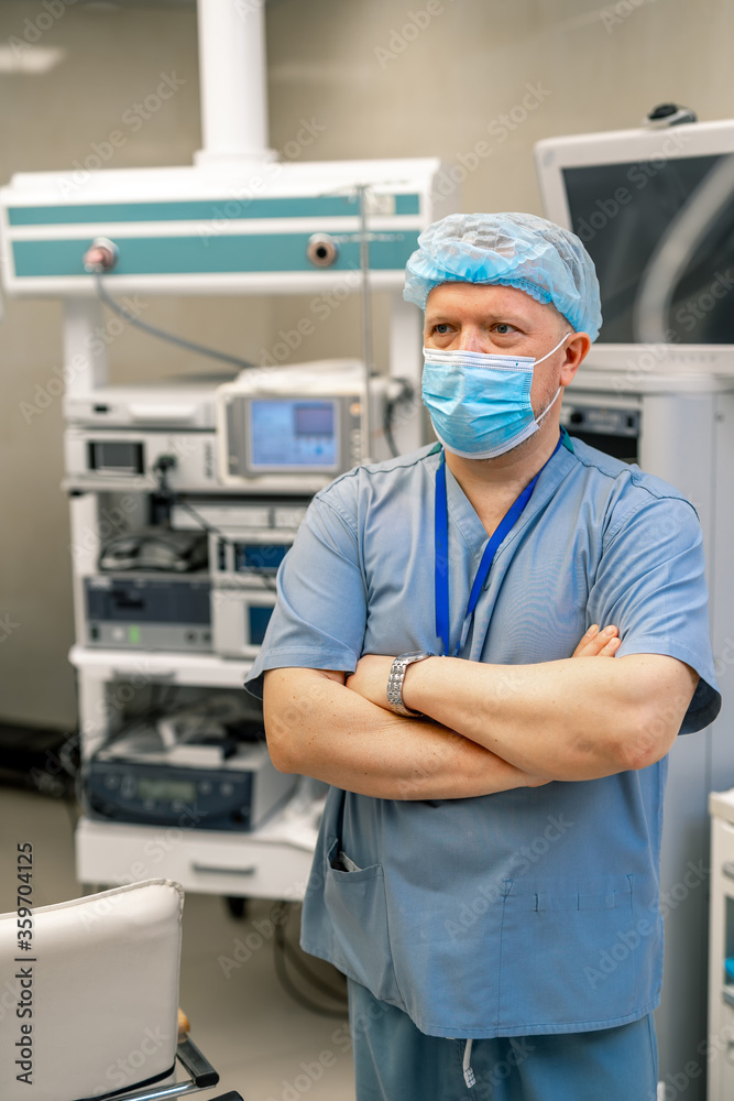 Naklejka premium Adult doctor standing cross hands in surgery room. Special modern equipment on the background.
