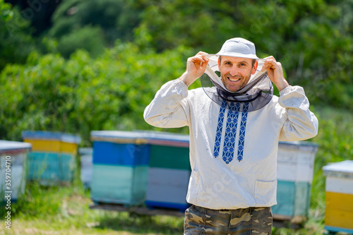 Beekeeper in protective workwear. Hives background at apiary. Works on the apiaries in the spring