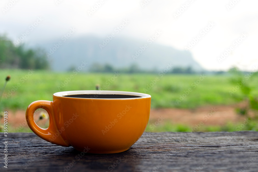 Black hot coffee drink on an old wooden table with a grass field and mountain nature landscape Black hot coffee drink on an old wooden table with a grass field and mountain nature landscape