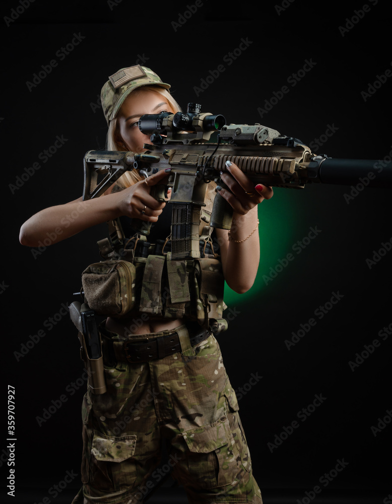 a sexy girl in military airsoft overalls poses with a gun in her hands on a dark background a sexy girl in military airsoft overalls poses with a gun in her hands on a dark background