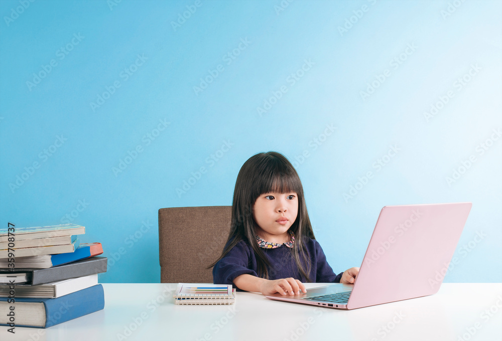Smart little girl using a laptop searching and studying on table, isolated on blue background. Education concept learning. Smart little girl using a laptop searching and studying on table, isolated on blue background. Education concept learning.