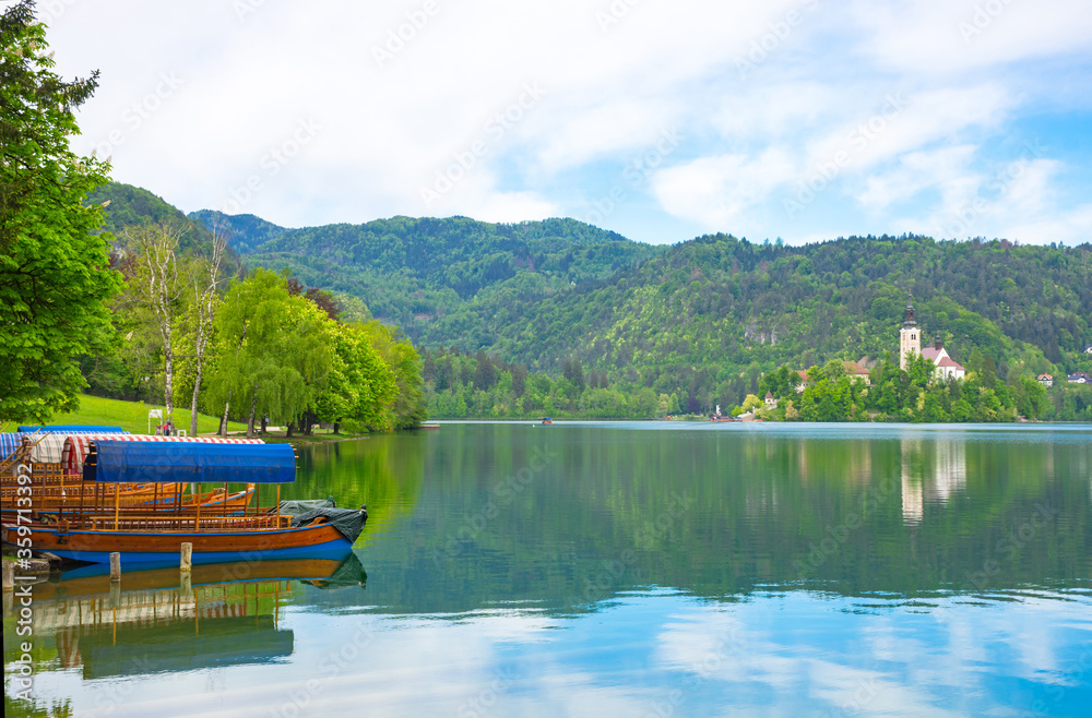 Fototapeta premium Traditional Pletna boat waiting for tourists on Lake Bled, with the lake island and charming little church in the background, famous tourists attraction in Slovenia
