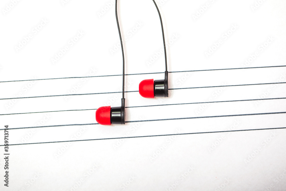 World music day concept. A pair of earphones placed on a staff drawn on a notepad simulating musical notes. World music day concept. A pair of earphones placed on a staff drawn on a notepad simulating musical notes.