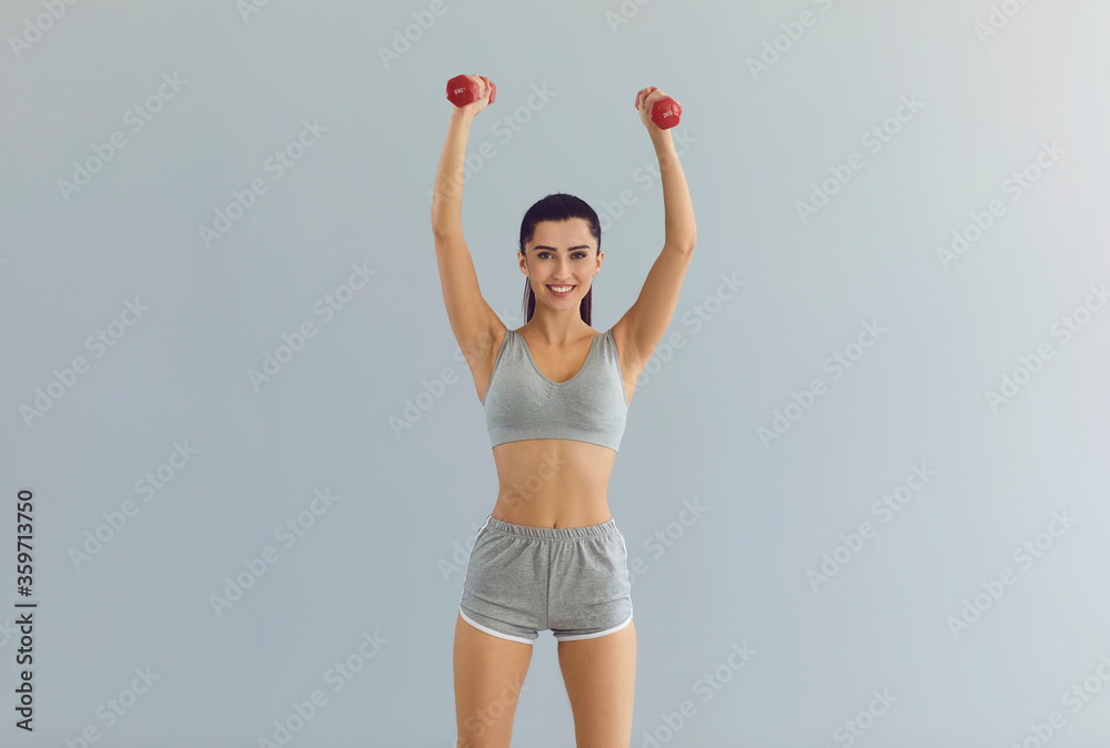 Sporty girl lifting dumbbells on grey background. Beautiful young fitness instructor working out with weights Sporty girl lifting dumbbells on grey background. Beautiful young fitness instructor working out with weights