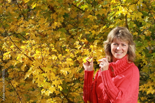 Happy senior woman with red pullover in front of autumn leaves