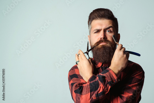 Barber with straight razor and scissors over blue background. Brutal man holding proffecional tools. Barber shop. photo