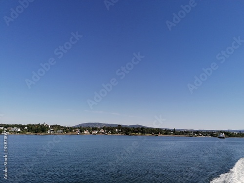 Beautiful calm day on the sea with clear blue sky and island with pine trees © Kristoffer