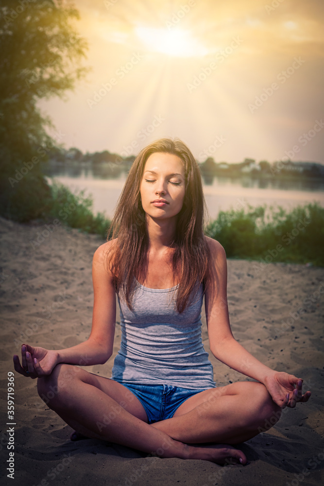 Nice lady is meditating on the sand with her legs crossed and eyes closed