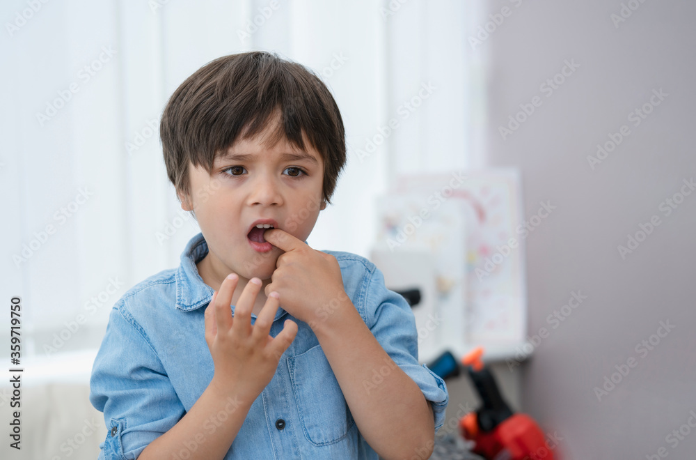 Portrait young kid putting finger in his mounth feeling hurt from falling first tooth,Emotional child boy standing alone with thinking face or nervous, Health care or Mental health Portrait young kid putting finger in his mounth feeling hurt from falling first tooth,Emotional child boy standing alone with thinking face or nervous, Health care or Mental health