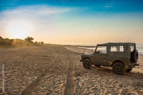 Vintage jeep parked on a deserted beach at sunrise in summer time , clear sky with no clouds , holiday scene photo