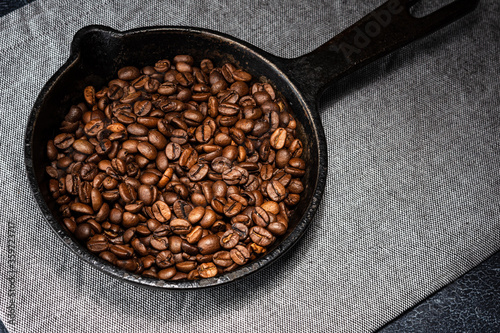 Freshly roasted coffee beans in a cast iron skillet. Linen napkin. A natural stone. Dark background.