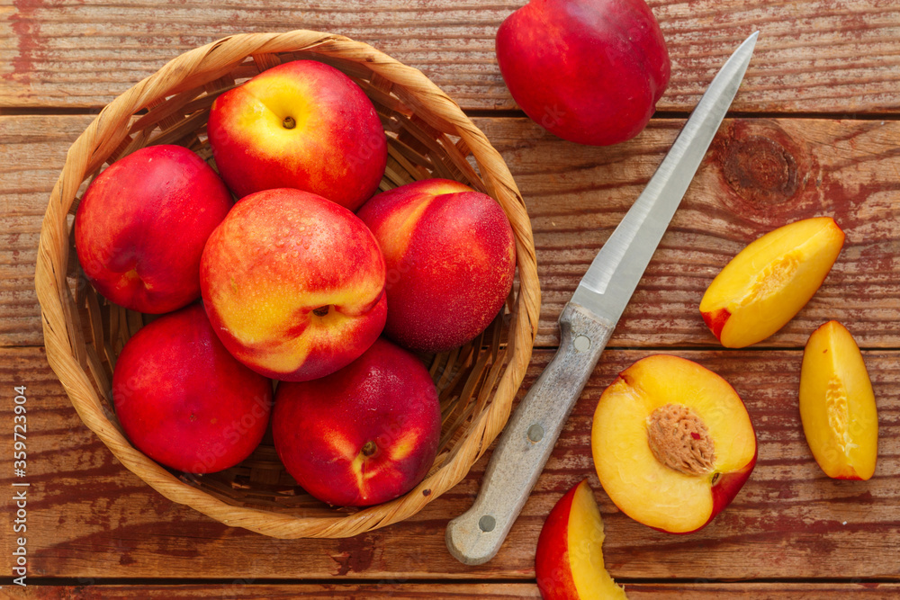 Nectarine. Ripe juicy organic nectarines (peaches) in a wicker basket. Whole and sliced fruit on a wooden table. Selective focus, top view, copy space Nectarine. Ripe juicy organic nectarines (peaches) in a wicker basket. Whole and sliced fruit on a wooden table. Selective focus, top view, copy space
