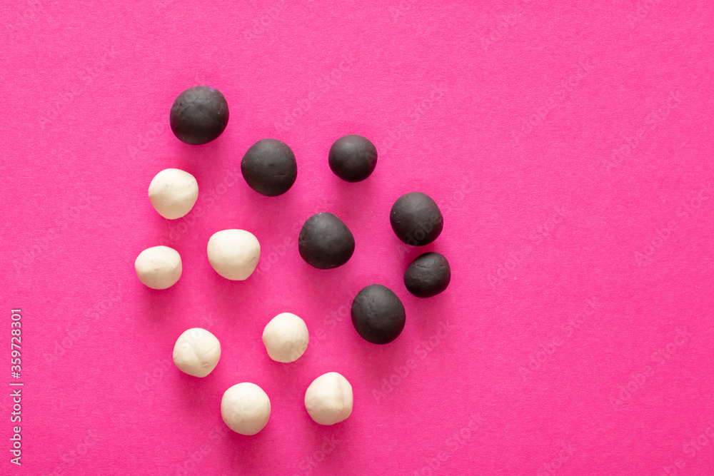 Group of white and black plasticine balls on pink vibrant background. Concepts of racism, group separated representing intolerance and conflict Group of white and black plasticine balls on pink vibrant background. Concepts of racism, group separated representing intolerance and conflict