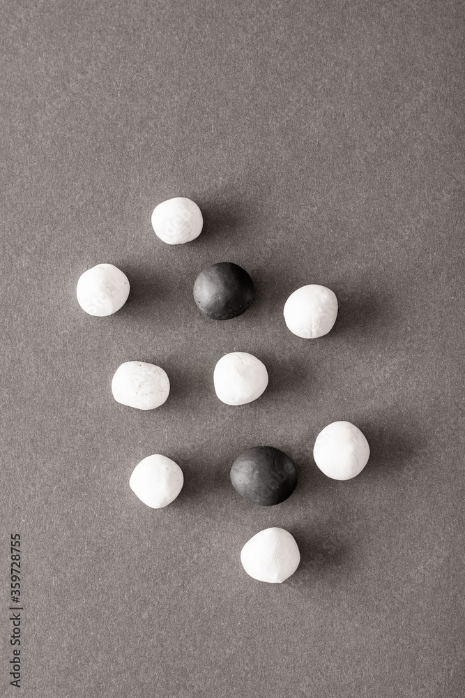 Black and white plasticine balls mixed on a grey background surface. Concepts of unity and togetherness, more white balls than black balls