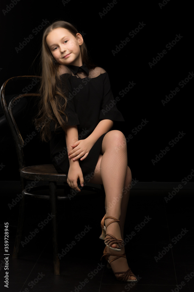Naklejka premium Portrait of a little girl sitting on an old Viennese chair, black background.