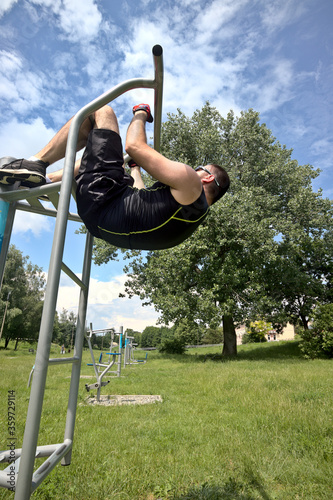 A young man in sports outfit trains abdominal muscles at an outdoor gym in the city park photo