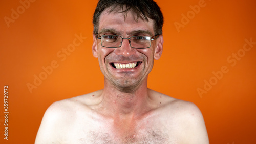 Mature man with glasses smiling on orange background. Portrait of adult laughing male with naked body.