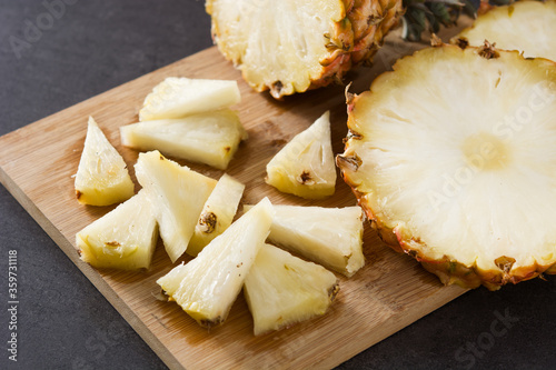Fresh pineapple slices on cutting board and black stone background