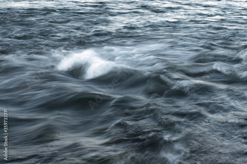 The stream of water, blurred view. Powerful water flow with breakers on the sea