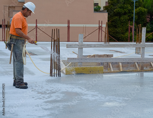Construction worker watering fresh concrete slab using a hose