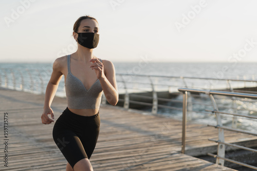 beautiful woman runs early in the morning along the promenade. A medical mask is worn on the face. Virus protection during an epidemic © mtrlin