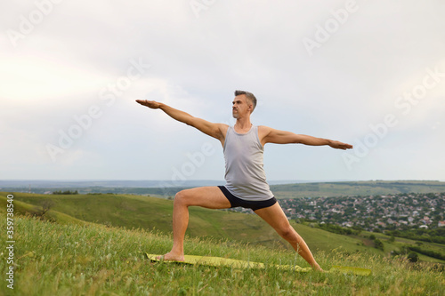 Mature man doing yoga exercise Valence on green grass in nature.