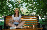 A girl in a hat sits on a park bench.